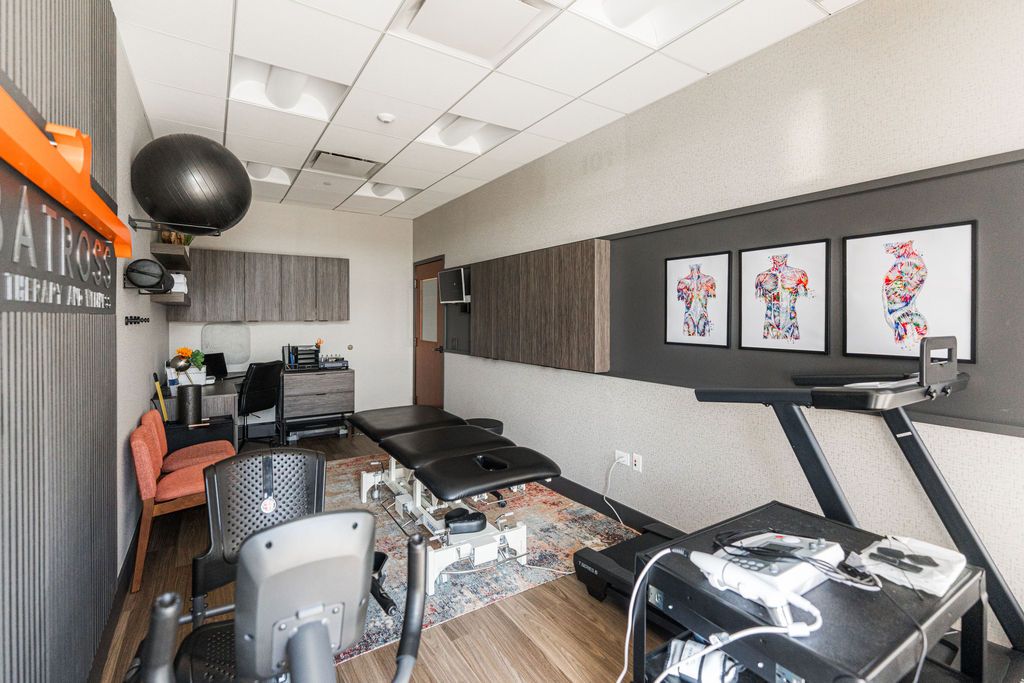 Albatross Physical Therapy Naperville — rehab floor with exercise bike, treadmill, therapy tables, and anatomical wall art