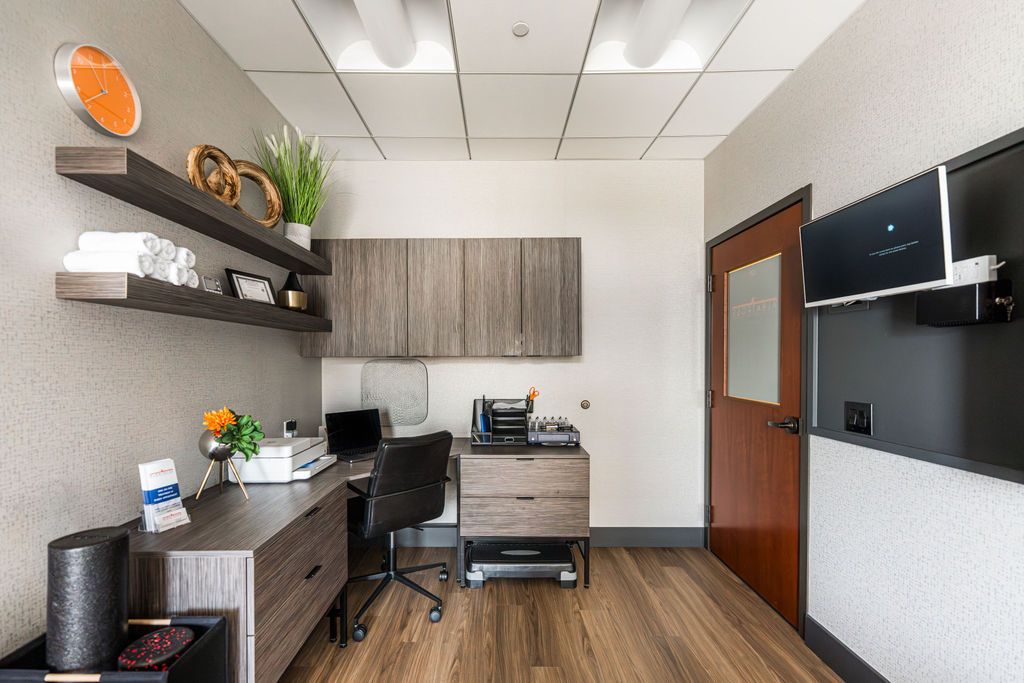 Albatross Physical Therapy Naperville — clinical consultation workspace with walnut-grain cabinetry, floating shelves, and wall-mounted TV