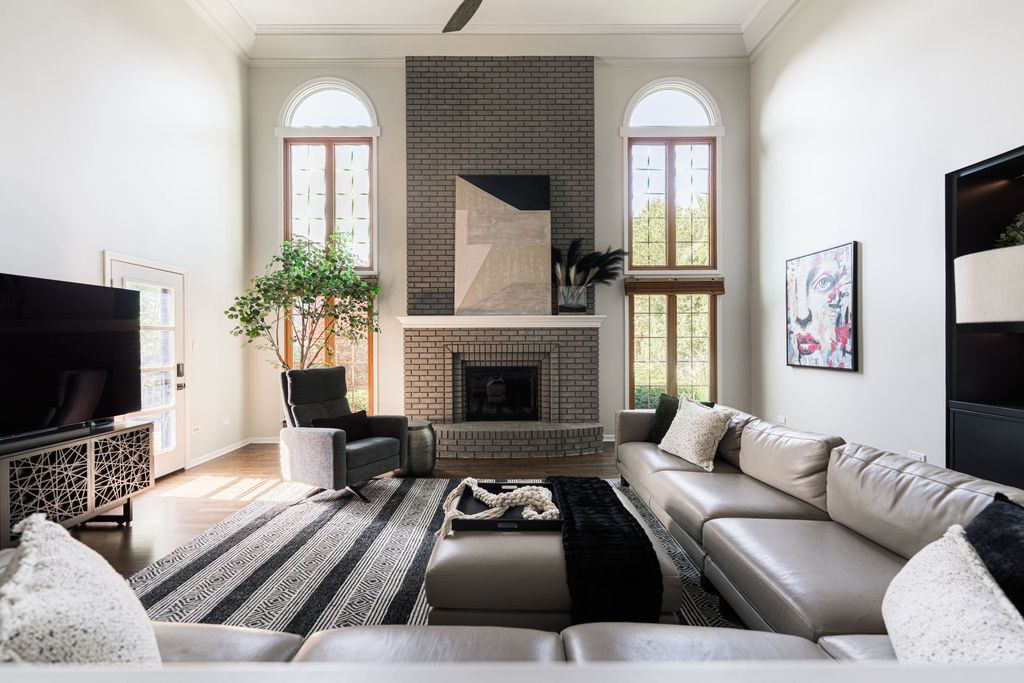 Alyssa Naperville living room — two-story great room with grey-painted brick fireplace wall, arched windows, and custom black built-in shelving