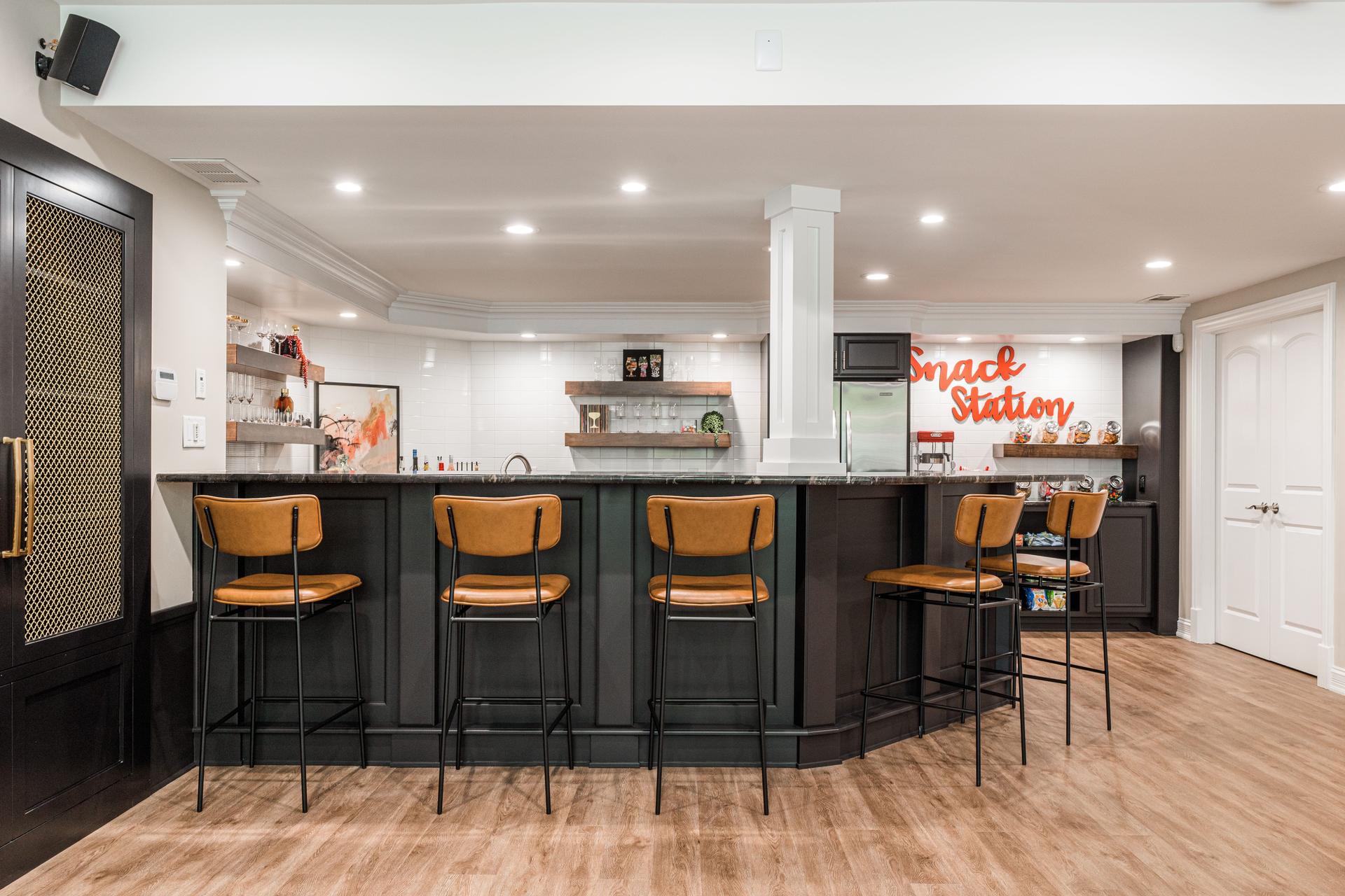 Basement bar and snack station overview — curved dark bar with black granite, leather stools, subway tile, and lit floating shelves — Geneva IL