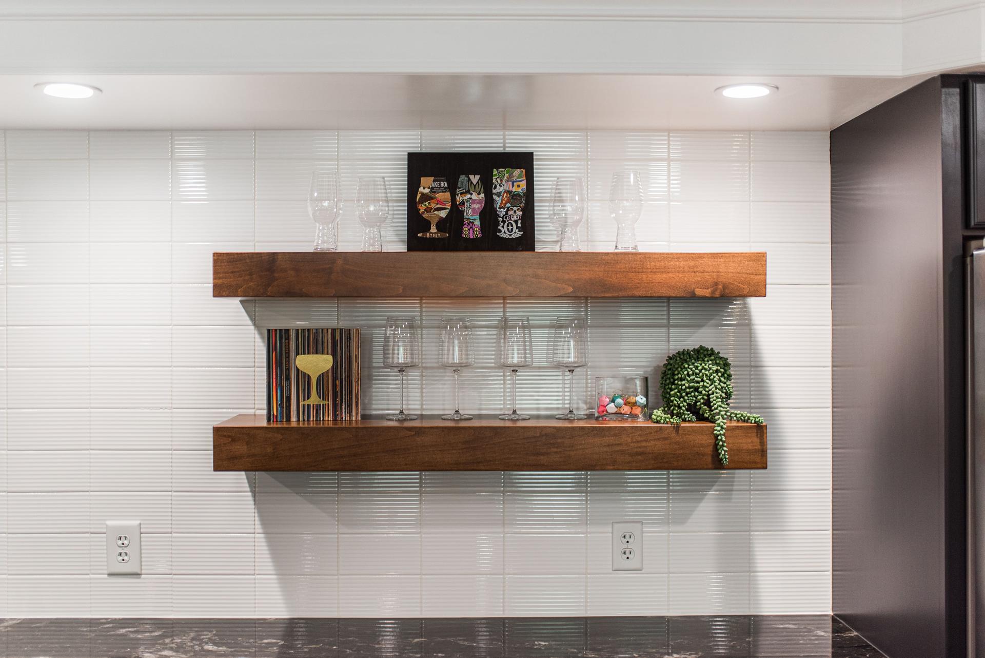 Walnut floating bar shelves with stemware display and textured white subway tile backsplash — Bealer basement bar Geneva IL