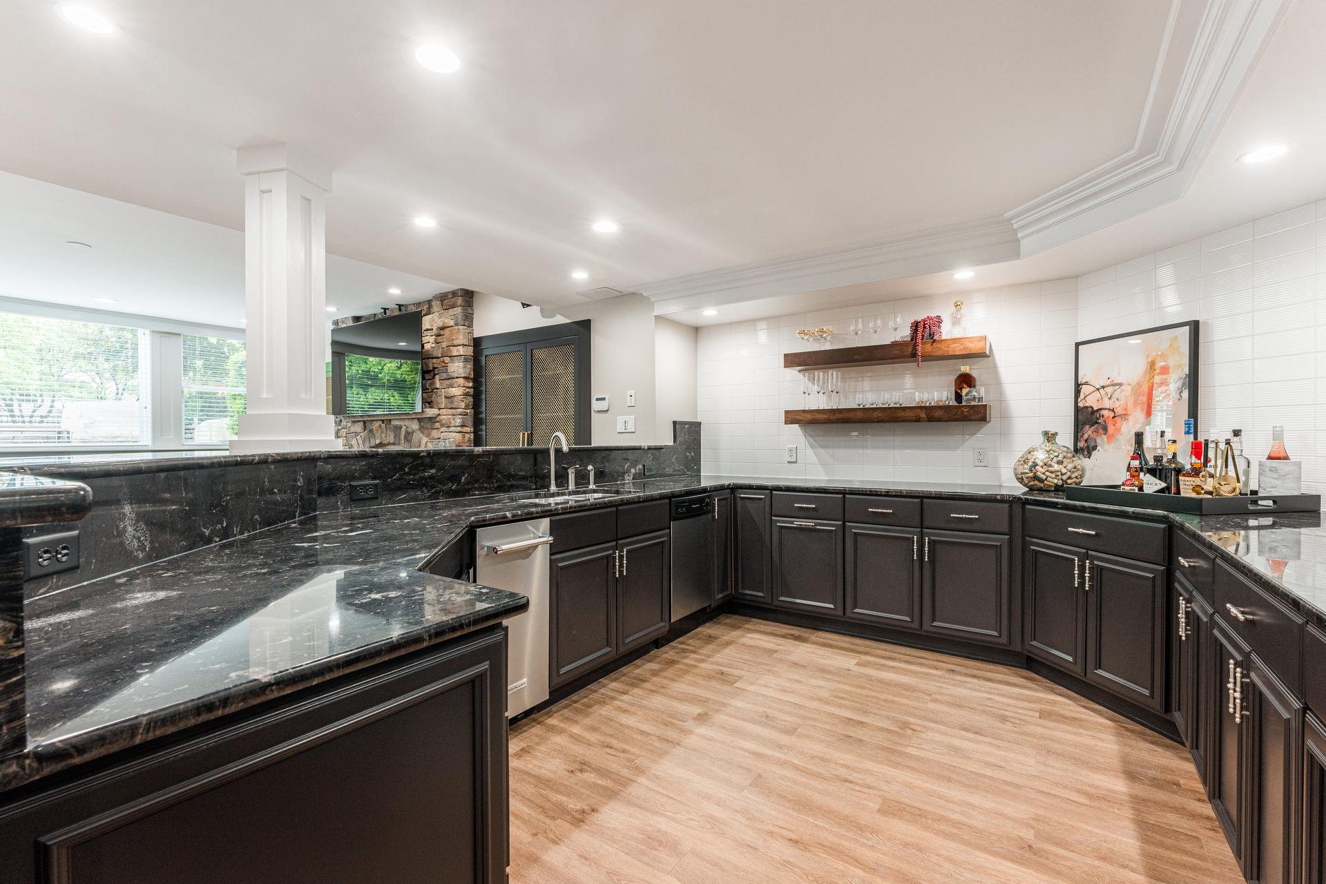Full wet bar detail — wraparound dark cabinetry, black granite countertops, dishwasher, and walnut floating shelves — Bealer basement Geneva IL