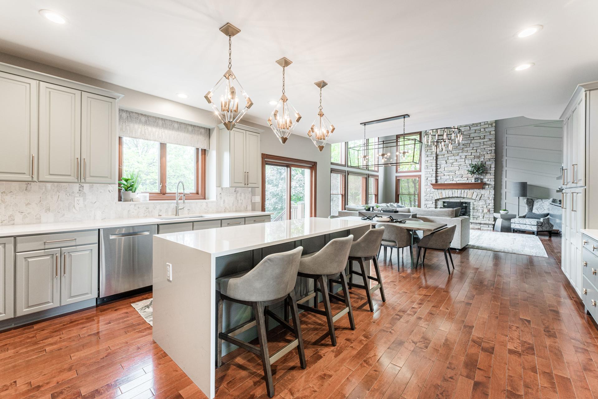 Kitchen and great room — gray cabinetry, sage island, extended quartz countertop, geometric gold pendants, and stone fireplace great room — Bealer Geneva IL