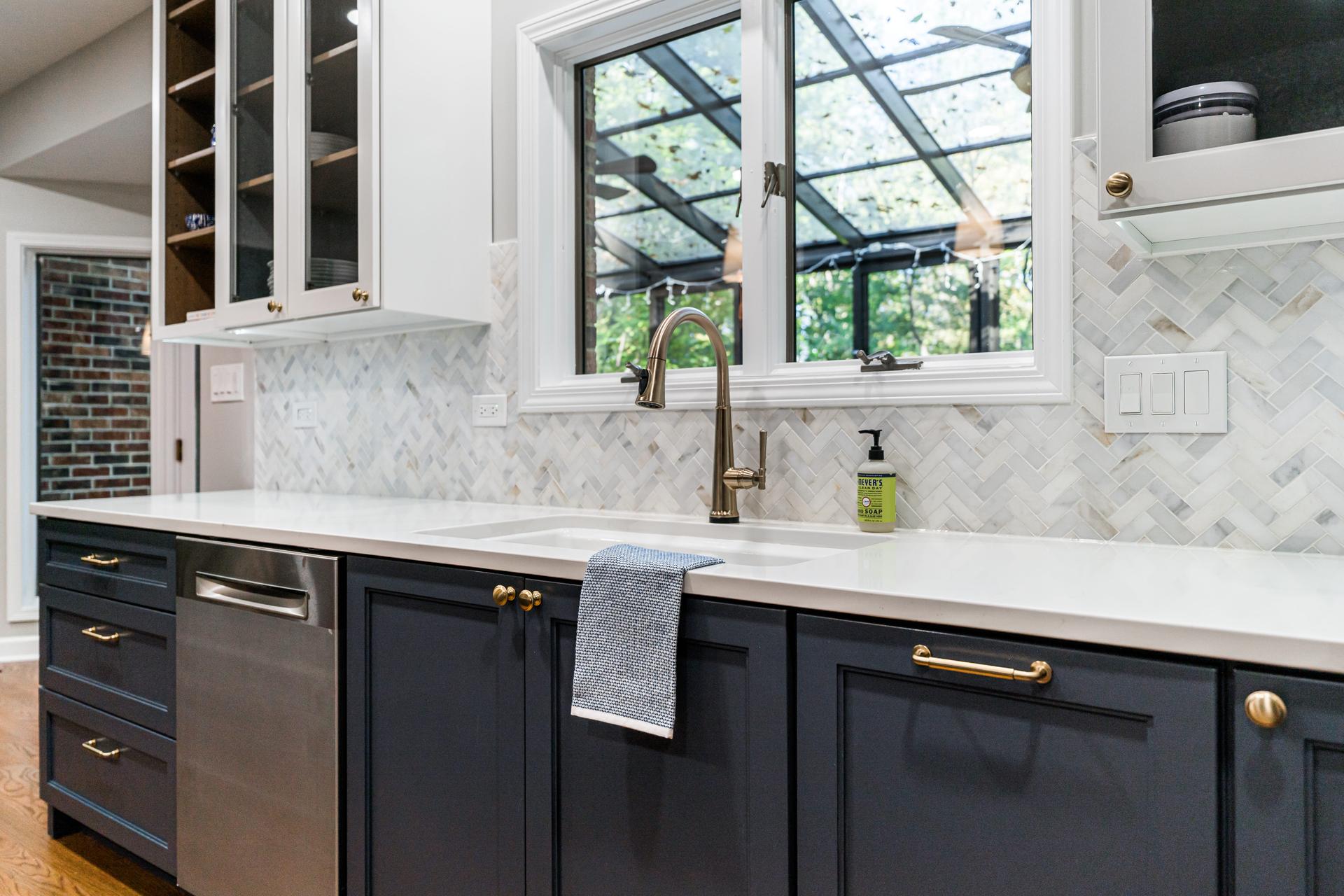 Sink wall — navy lower cabinets, white glass-front uppers, marble herringbone tile, champagne bronze faucet — Shorewood IL kitchen remodel