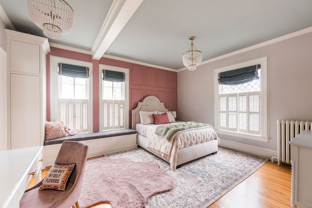 Fulton Geneva girl's bedroom — pink paneled accent wall, grey ceiling, beaded chandelier, custom window bench, and built-in wardrobe