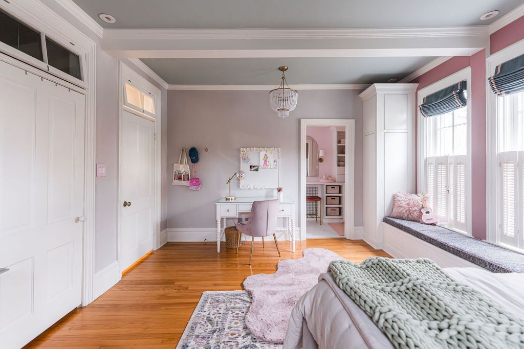 Fulton Geneva girl's suite — full bedroom with custom desk area, pink en-suite bathroom glimpse, window bench, and original wood floors