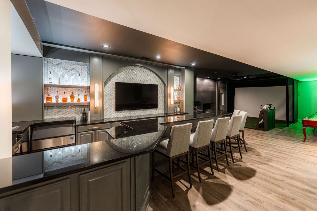 Hickory St. Charles basement — custom bar with black granite, herringbone tile, arched TV niche, and golf simulator in background