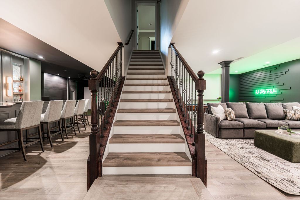 Hickory St. Charles — staircase view showing full basement open plan with bar on left, lounge on right, and golf simulator glow