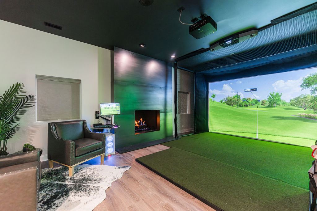 Hickory St. Charles — golf simulator room with projector, turf mat, fireplace, leather club chair, and live course on screen