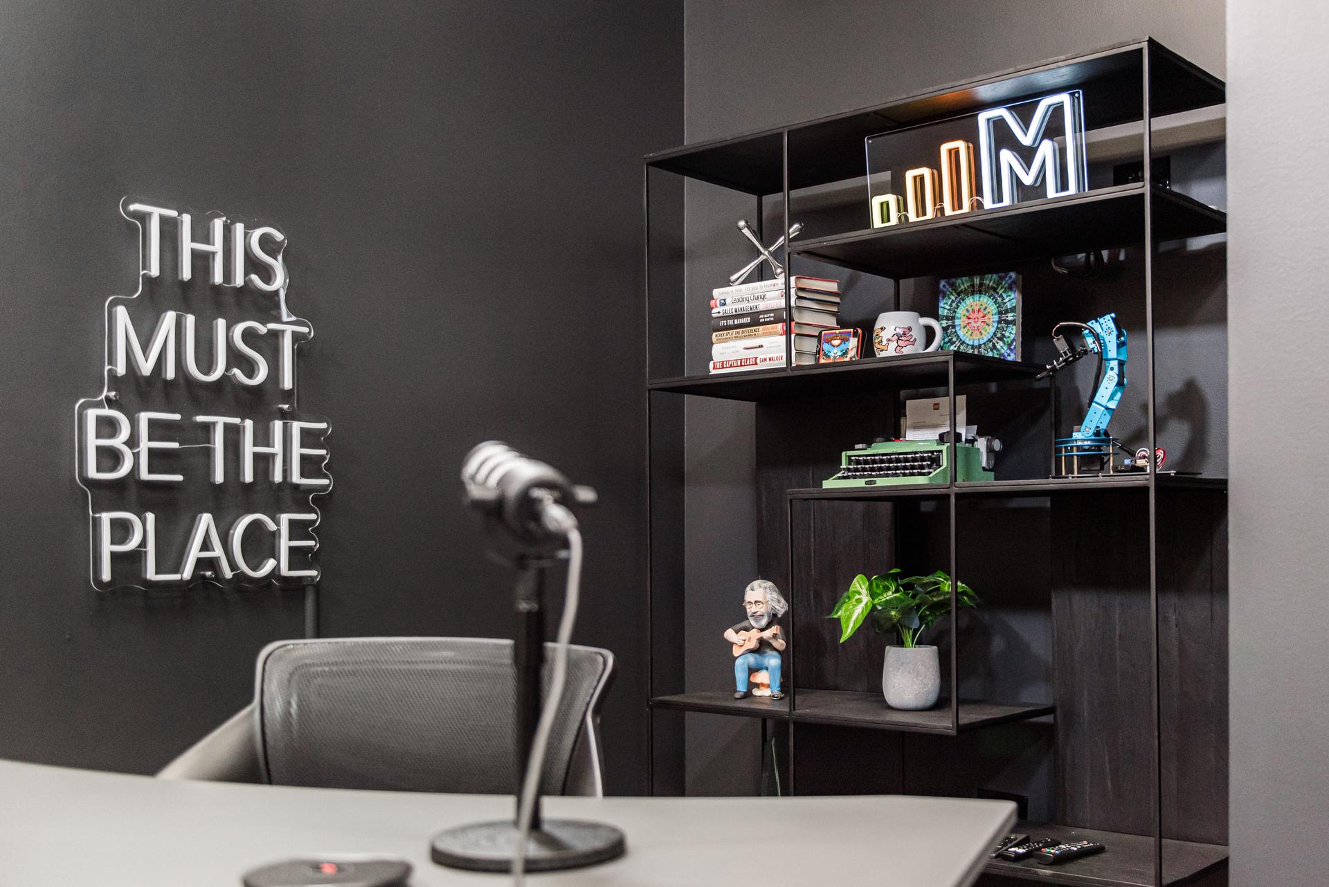 Podcast studio detail — professional microphone setup, neon signage, and custom display shelving — MRG Naperville