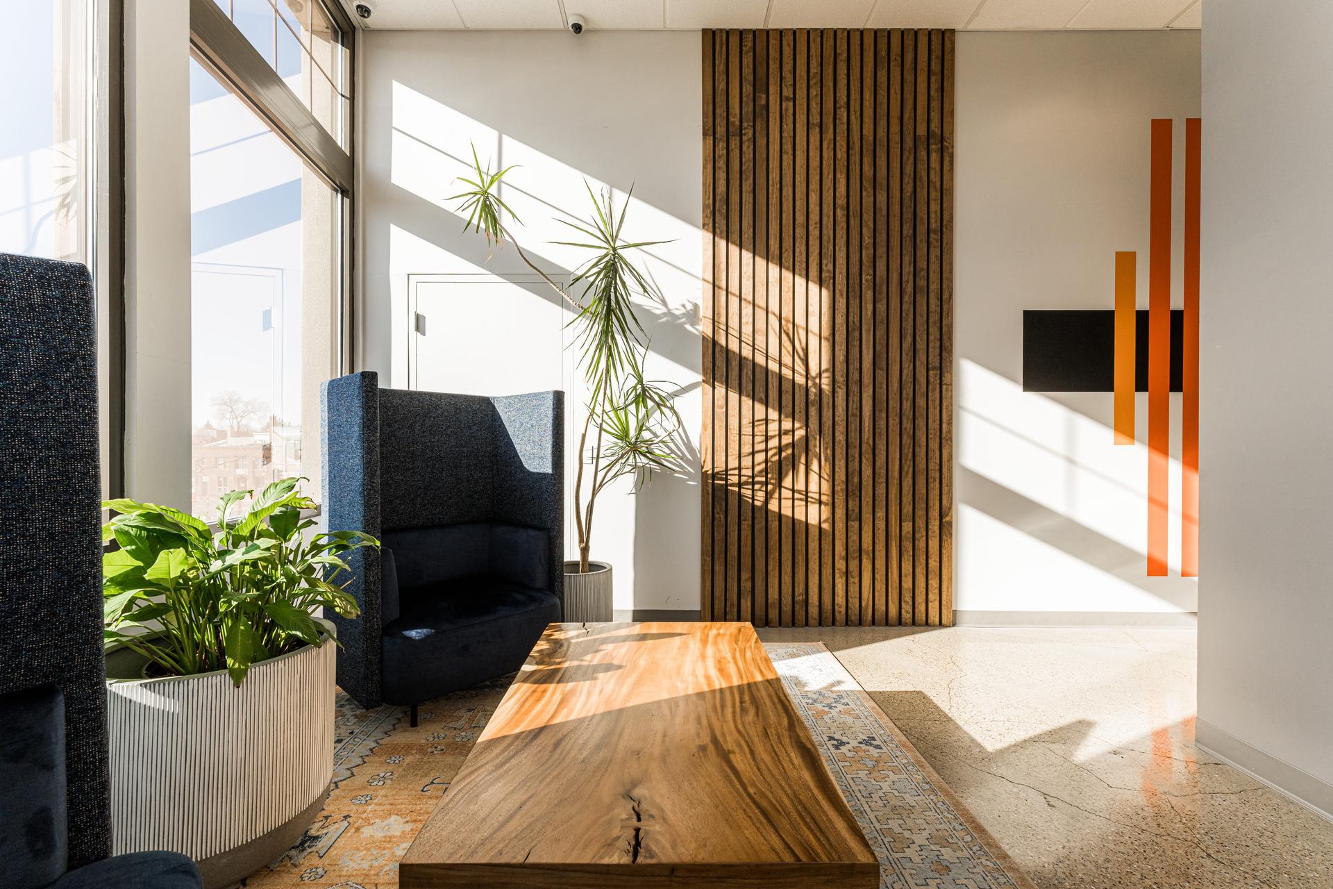 Natural light lounge zone with live-edge coffee table, slatted wood accent wall, and custom art installation — MRG Naperville