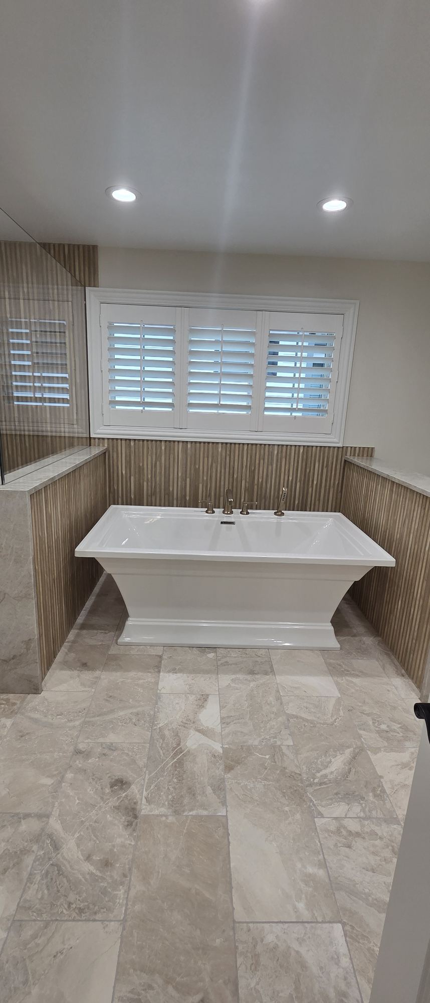 Park Ridge primary bathroom — freestanding soaking tub under plantation-shuttered windows with fluted wood-look tile and marble ledges