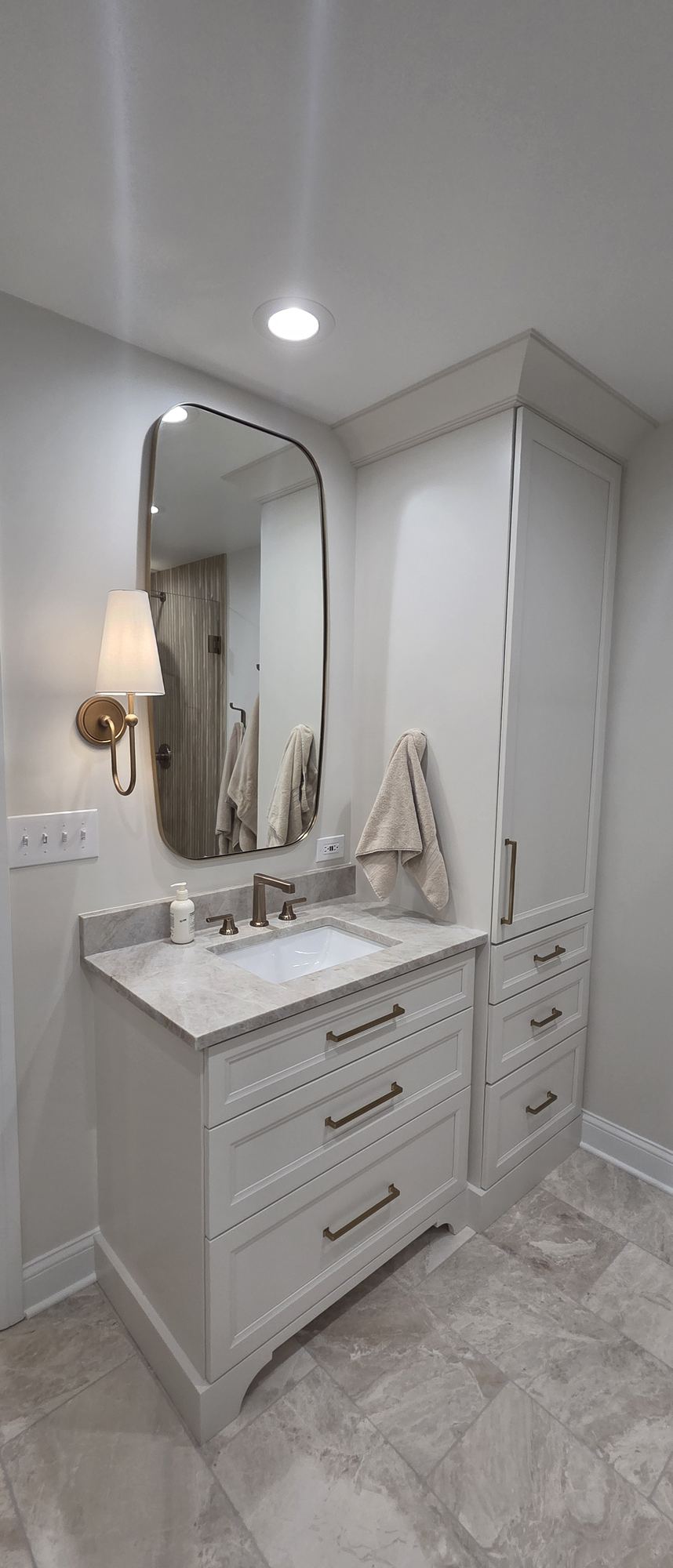 Park Ridge primary bathroom — second vanity with curved brass-framed mirror, brass sconce and linen tower